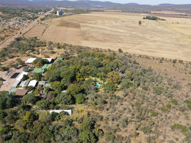 An aerial view of the property showing multiple buildings, a swimming pool, and surrounding landscape with access to the main road.