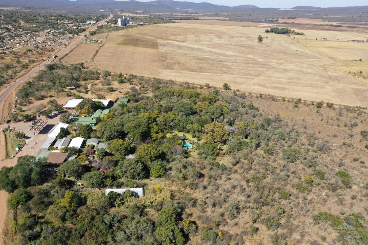 An aerial view of the property showing multiple buildings, a swimming pool, and surrounding landscape with access to the main road.