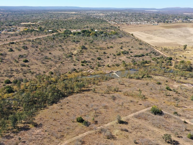 An aerial view of a large, undeveloped rural plot featuring natural vegetation, a river running through the property, and an unpaved access road.