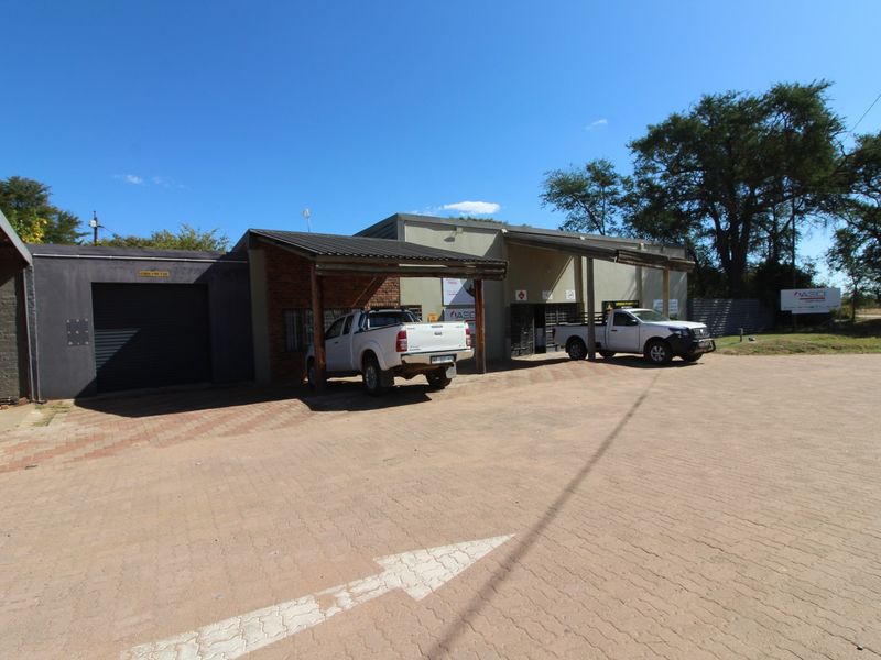 Front exterior view of a commercial retail property featuring a paved driveway, covered parking bays, and a roller shutter door entrance.