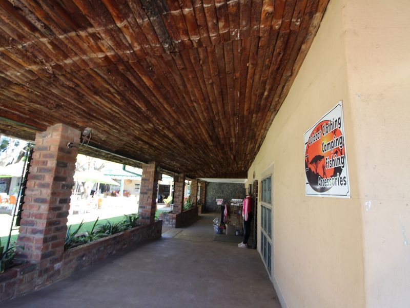 A covered outdoor walkway featuring a rustic timber ceiling, face brick support pillars, and a built-in brick planter box, suitable for retail display.