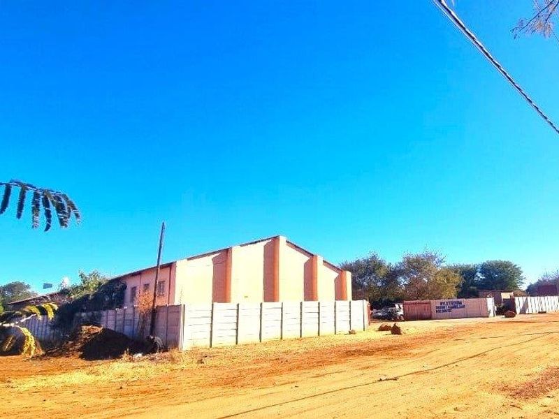 Street view of an industrial property featuring a precast concrete boundary wall and an unpaved access road.