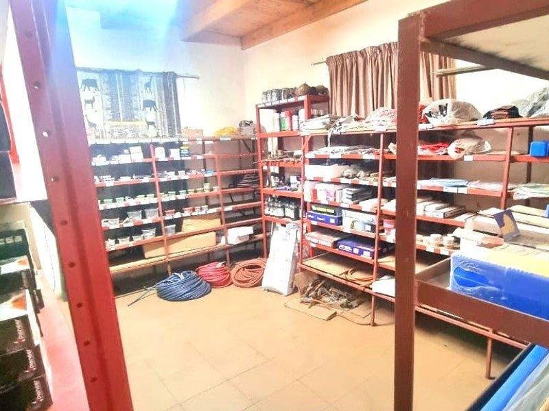 A functional industrial utility or storage space featuring exposed timber ceiling beams, tiled flooring, and extensive fixed metal shelving for organized storage.