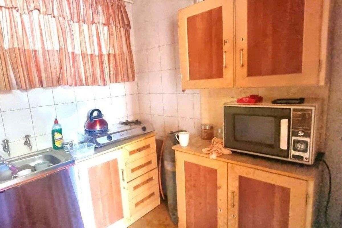 A compact industrial kitchen featuring built-in wooden cabinetry, a stainless steel sink, and a gas hob with tiled backsplash.