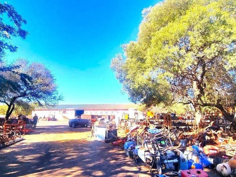 An industrial property featuring a large warehouse building set within a spacious, unpaved yard area surrounded by mature trees.