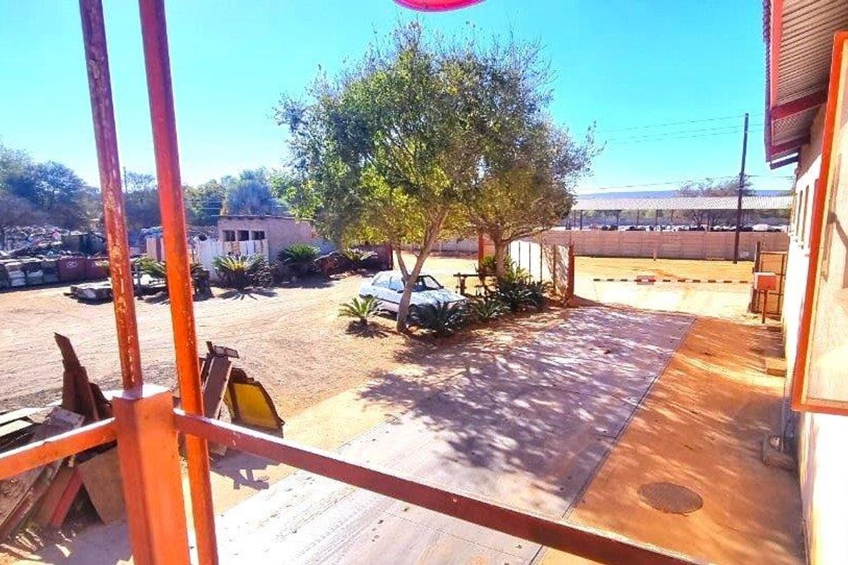 An industrial rear yard area featuring a concrete surface, perimeter walling, and metal structural supports for the building overhang.