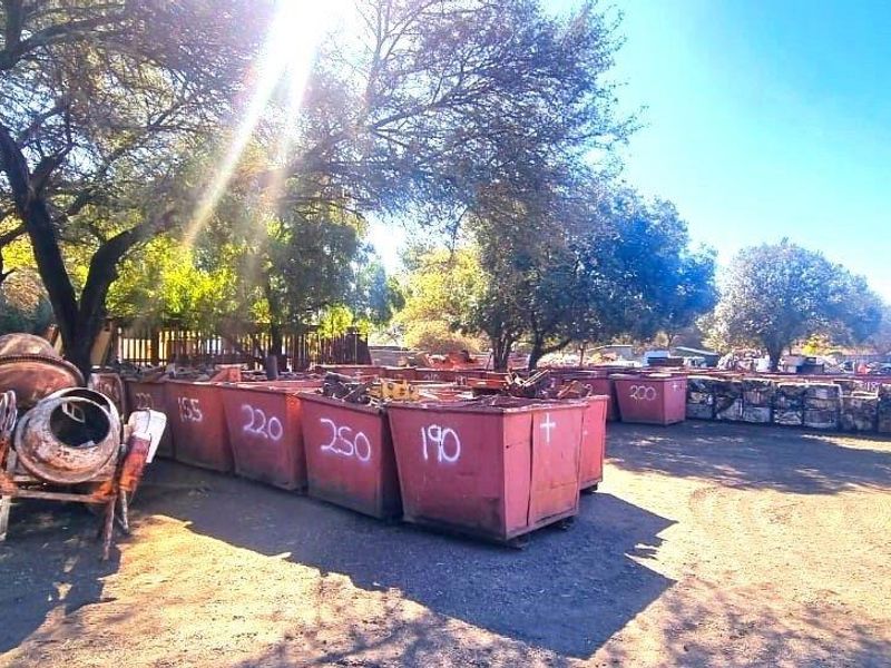 An industrial outdoor yard area featuring unpaved ground and mature trees, currently utilized for storage of industrial containers and equipment.