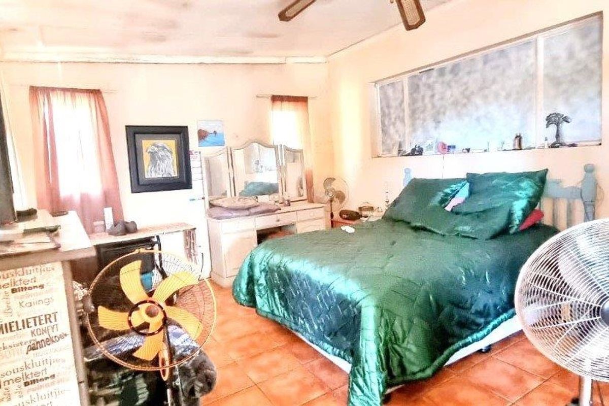 A bedroom featuring tiled flooring and a ceiling fan, showing signs of wear including ceiling staining and window frame deterioration.