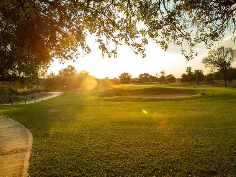 A scenic view of a well-maintained landscaped garden area featuring a paved walkway and a sand bunker at sunset.