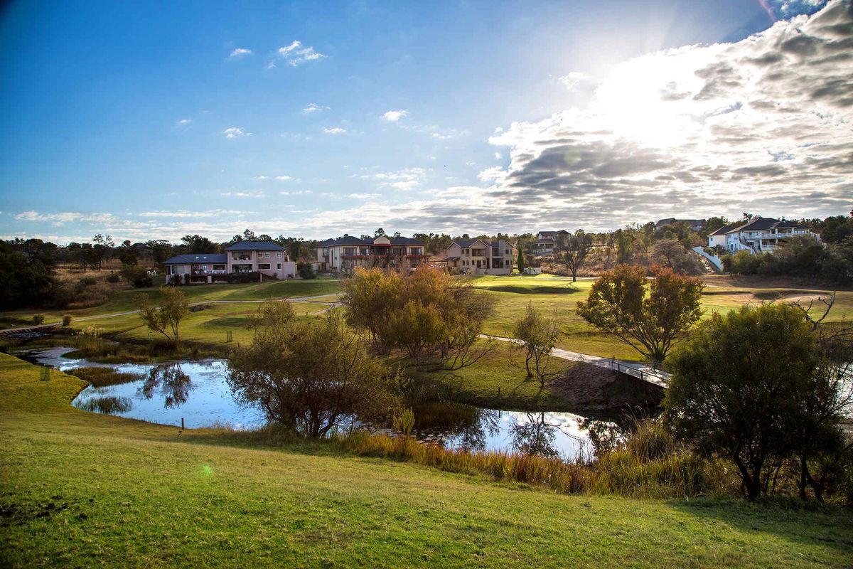 A scenic view of the landscaped estate grounds featuring a tranquil pond, pedestrian bridge, and surrounding residential properties.