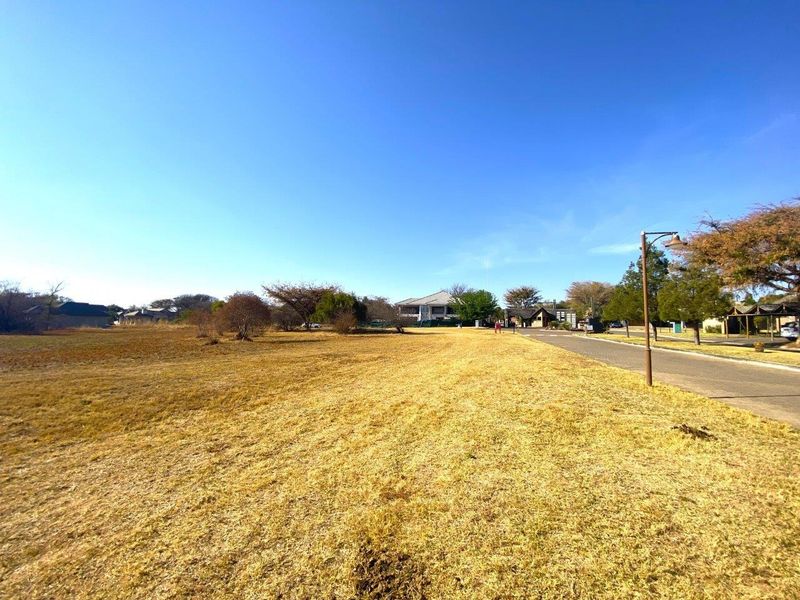 A wide-angle view of a vacant commercial land plot adjacent to a paved road with existing street lighting infrastructure.