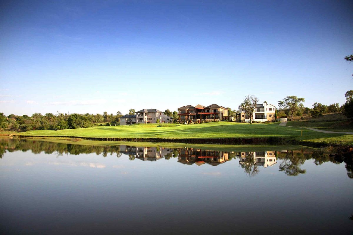 A scenic view of a golf course estate featuring manicured lawns and a tranquil water feature reflecting the surrounding residential properties.