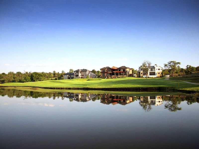 A scenic view of a golf course estate featuring manicured lawns and a tranquil water feature reflecting the surrounding residential properties.