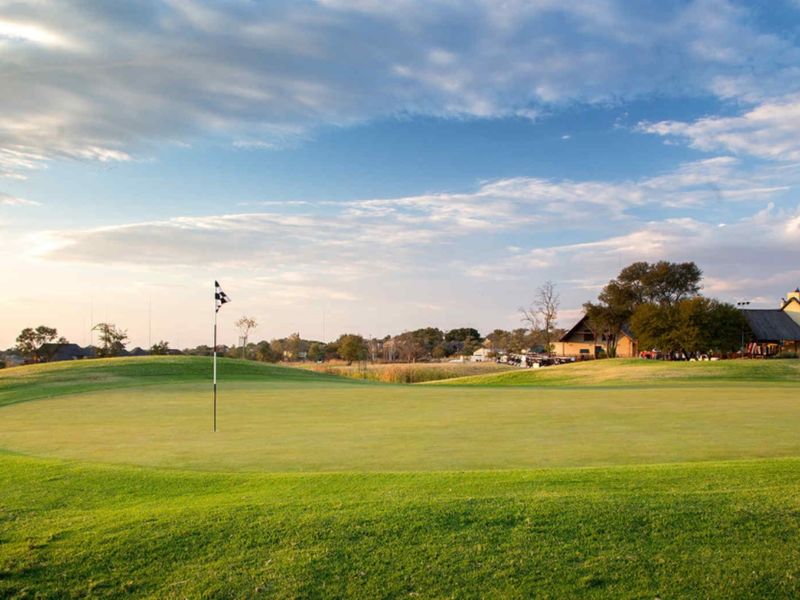 A scenic view of a well-maintained golf course green with a clubhouse visible in the background under a clear sky.