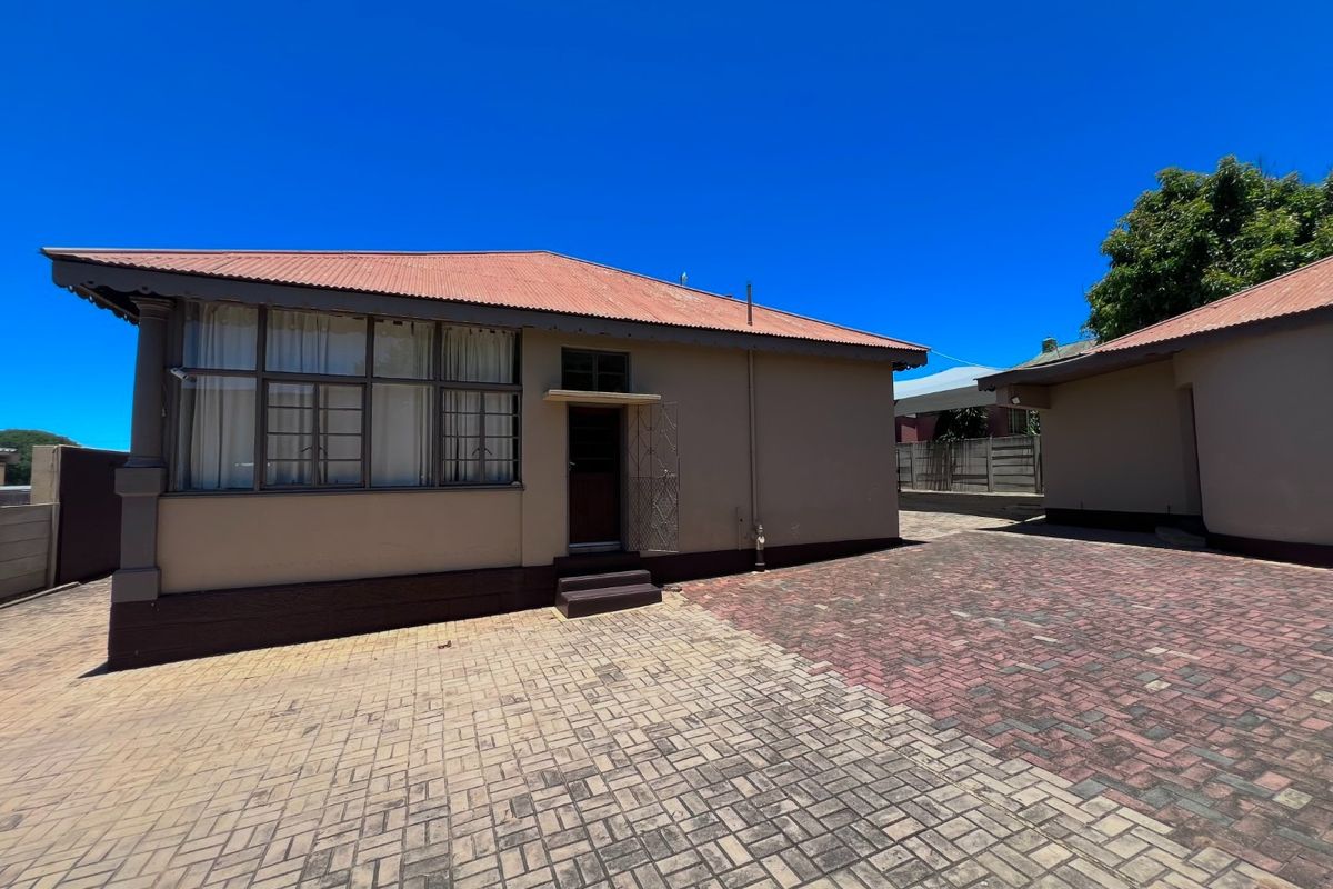 Rear exterior view of the property featuring a paved courtyard area and a building with a corrugated metal roof and steel window frames.