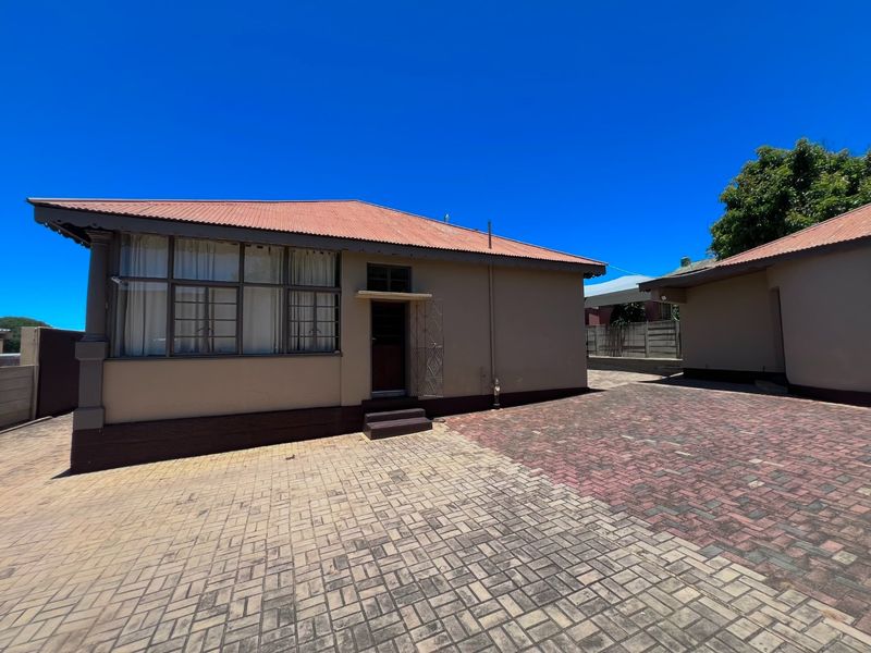 Rear exterior view of the property featuring a paved courtyard area and a building with a corrugated metal roof and steel window frames.