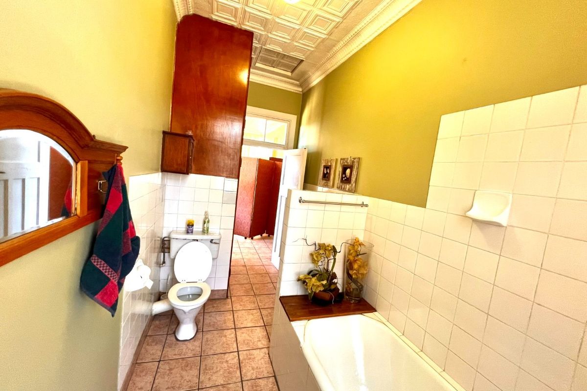 A dated bathroom featuring decorative ceiling tiles, wall tiling, a built-in bathtub, and a standard toilet, offering potential for a modern renovation.
