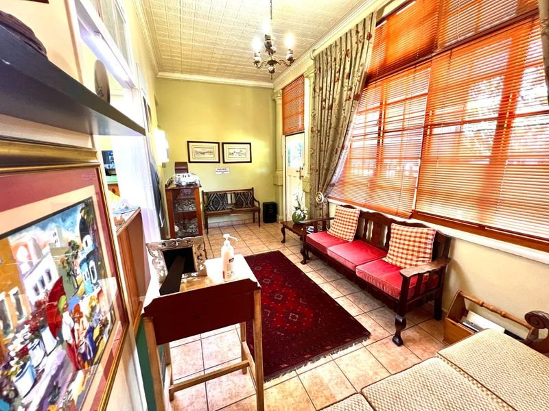 A waiting area or reception space featuring tiled flooring, a decorative pressed metal ceiling, and large windows with fitted blinds.