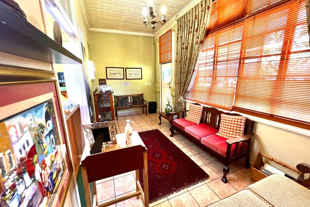 A waiting area or reception space featuring tiled flooring, a decorative pressed metal ceiling, and large windows with fitted blinds.