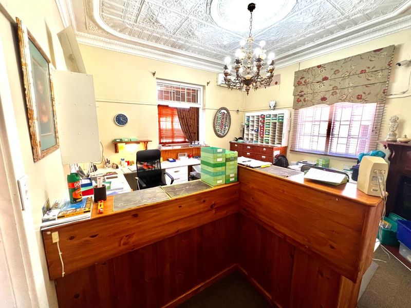 A functional office space featuring a built-in wooden reception desk, classic pressed metal ceiling, and integrated storage shelving.