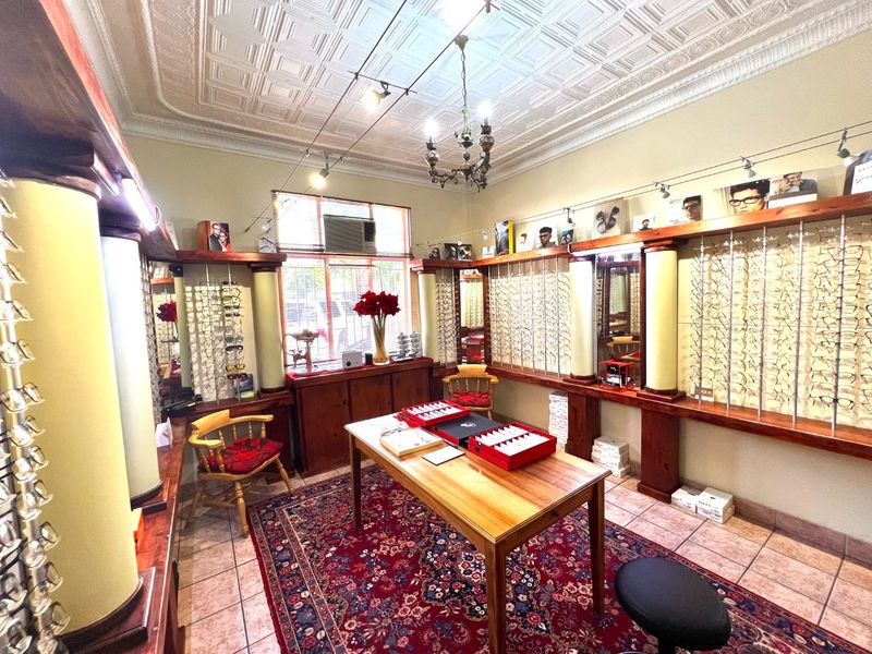 A well-maintained commercial office space featuring decorative ceiling tiles, built-in wooden display shelving, and integrated track lighting, currently utilized as an optical retail area.