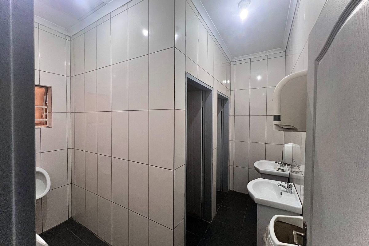 A functional commercial restroom facility featuring tiled walls, pedestal washbasins, and urinals, providing a clean and practical layout for business use.