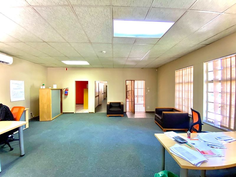 Spacious office area featuring a suspended ceiling, recessed lighting, air conditioning, and large windows with vertical blinds, providing a functional workspace environment.