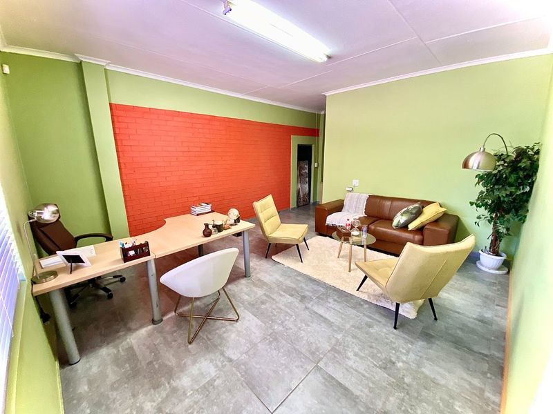 A functional office space featuring a distinctive orange exposed brick feature wall, neutral green painted walls, and durable tiled flooring throughout.