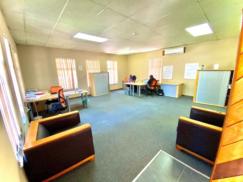 A functional open-plan office space featuring carpeted flooring, suspended ceiling tiles, recessed lighting, and wall-mounted air conditioning.
