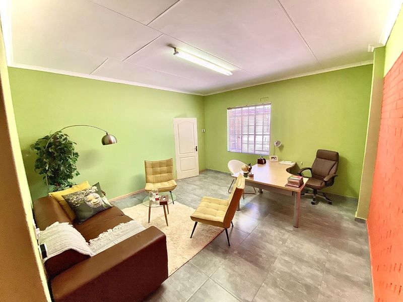 A functional office space featuring tiled flooring, green painted walls, and natural light through a window with venetian blinds.