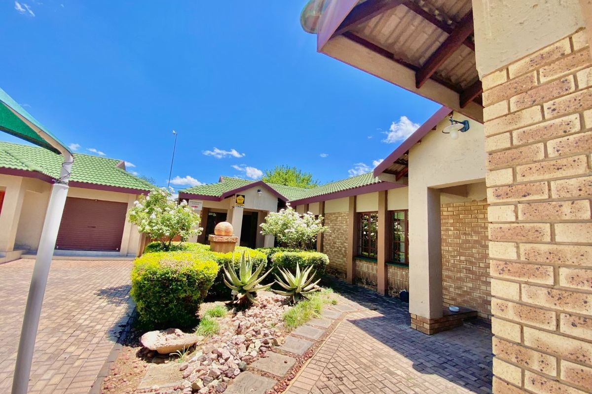 A well-maintained front exterior view featuring brick paving, landscaped garden beds, and a covered entrance walkway with face brick detailing.