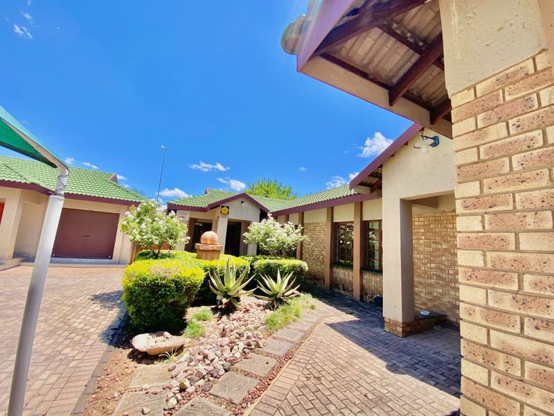 A well-maintained front exterior view featuring brick paving, landscaped garden beds, and a covered entrance walkway with face brick detailing.