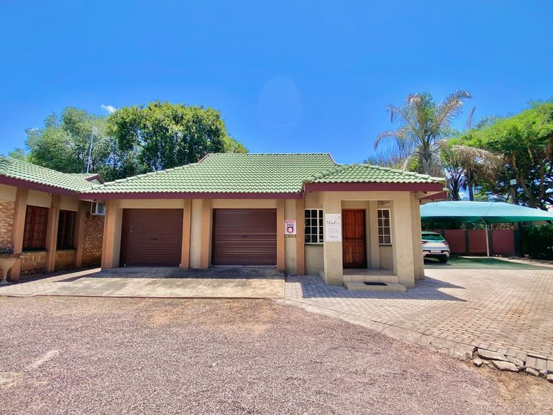 Front exterior view of a business property featuring a double garage, paved driveway, and a covered carport area.
