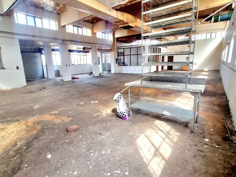 Spacious open-plan commercial industrial unit featuring high ceilings, exposed structural beams, large windows for natural light, and a central steel staircase.