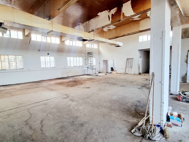 Spacious open-plan commercial area featuring exposed industrial ducting, concrete flooring, and structural columns, requiring significant refurbishment to restore its functional appeal.