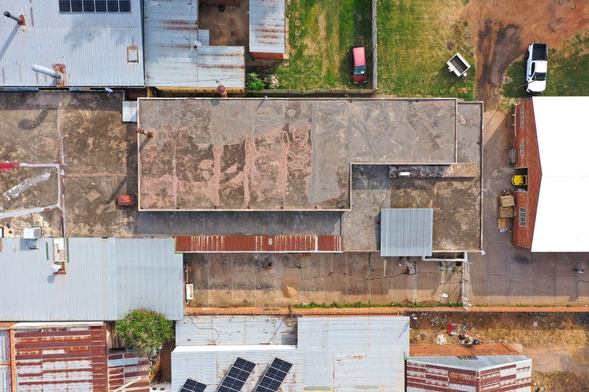 Aerial view of a commercial property complex featuring multiple buildings with corrugated metal and concrete roofing, solar panels, and paved yard space.
