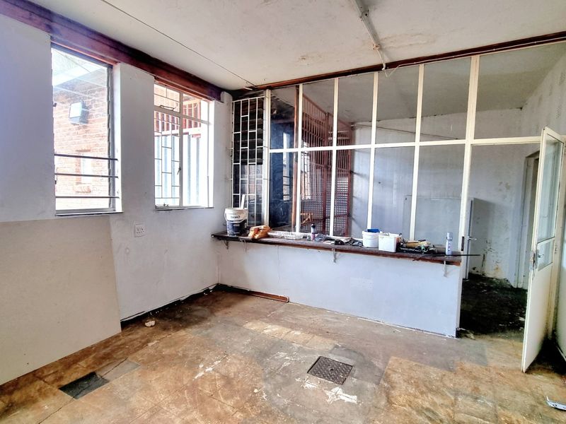 An empty commercial office space featuring tiled flooring, aluminium window frames with security bars, and a partition wall with a service counter.