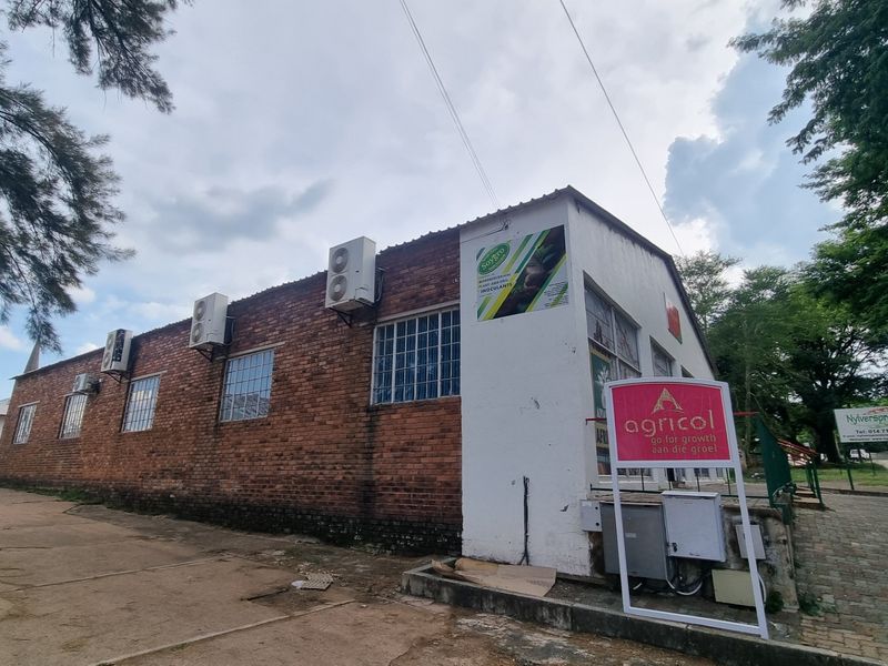 Commercial property exterior featuring exposed brick walls, multiple wall-mounted air conditioning units, and paved access area with prominent business signage.