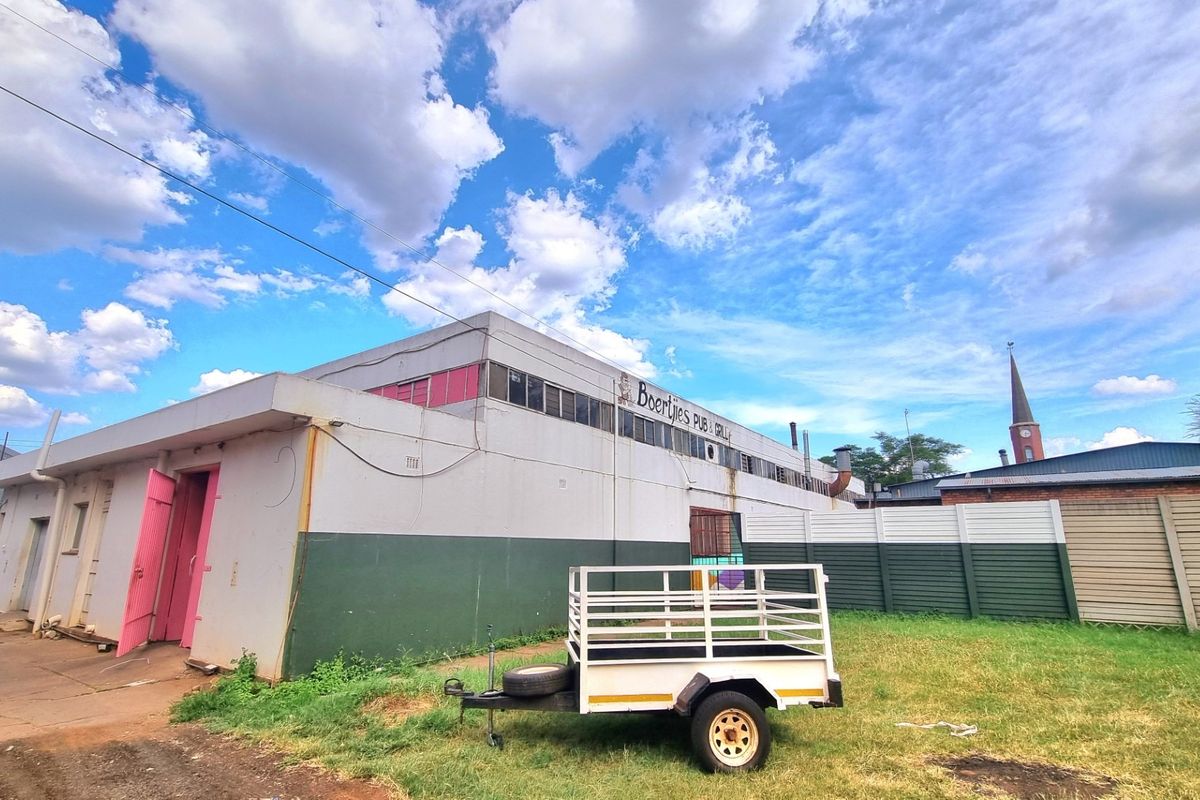 Rear exterior view of a commercial building featuring painted masonry walls, steel windows, and a surrounding fenced area.