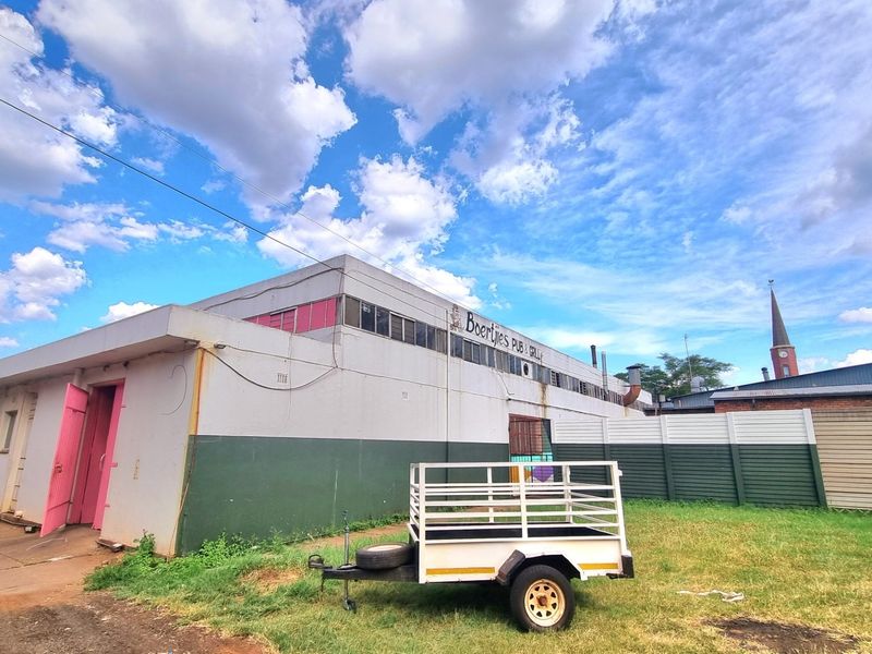 Rear exterior view of a commercial building featuring painted masonry walls, steel windows, and a surrounding fenced area.