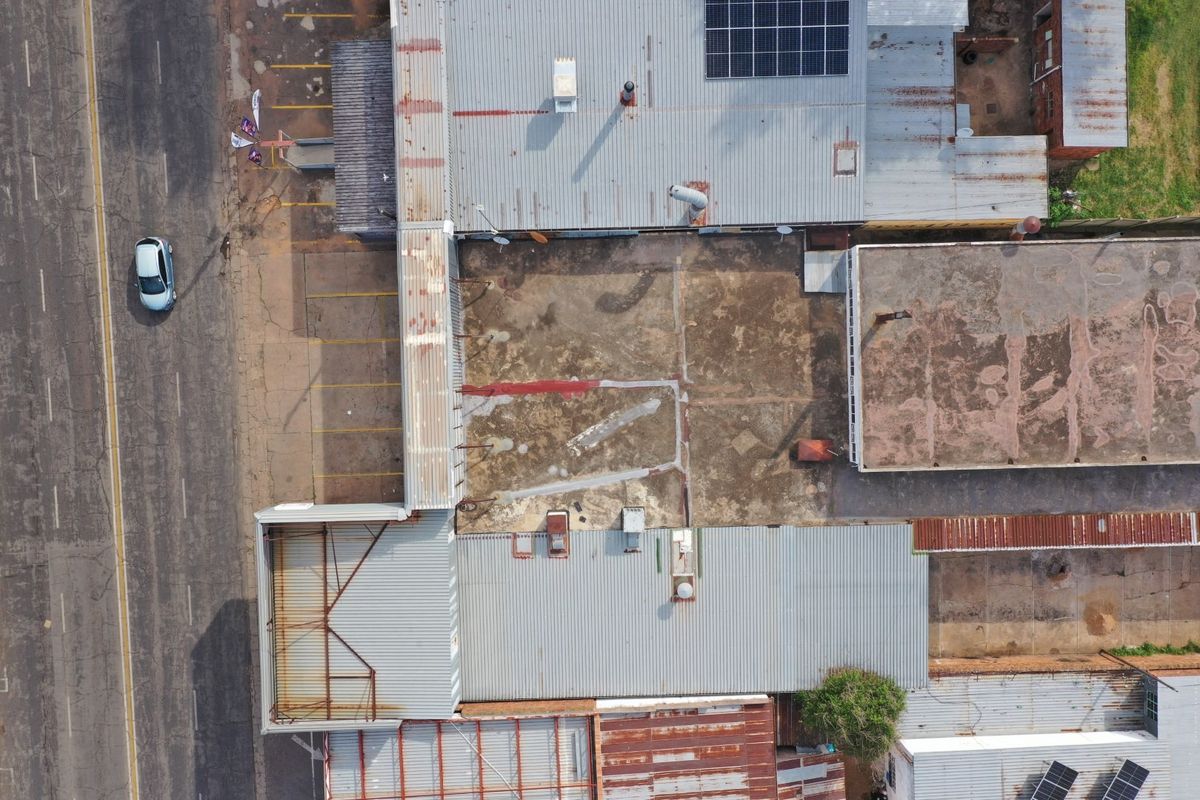 Aerial view of a commercial property featuring corrugated metal roofing, solar panel installation, and a large paved yard area showing signs of wear.