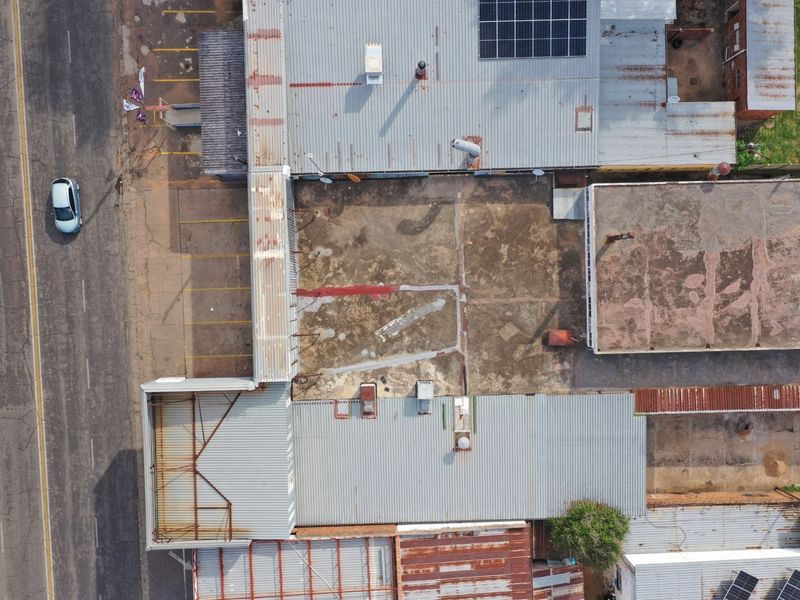 Aerial view of a commercial property featuring corrugated metal roofing, solar panel installation, and a large paved yard area showing signs of wear.