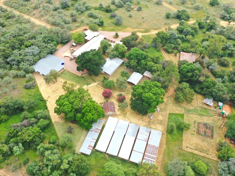 Aerial view of a farm property featuring multiple outbuildings with corrugated metal roofs, established trees, and various fenced enclosures across the landscape.