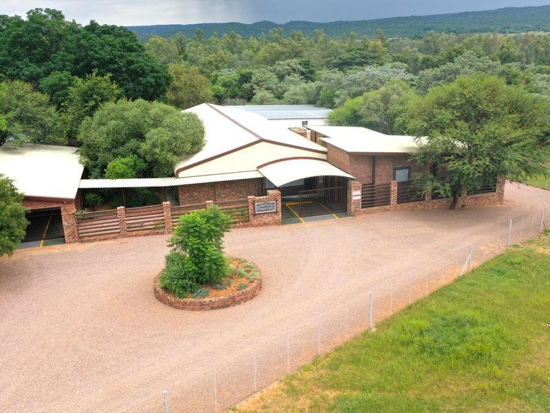 Aerial view of a brick farm property featuring a gravel driveway, covered entrance, and extensive surrounding greenery.