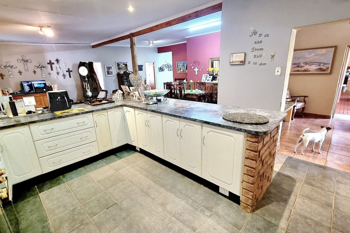 A functional kitchen featuring white cabinetry, laminate countertops, and a unique brick-supported breakfast bar, opening into the adjacent dining and living areas.