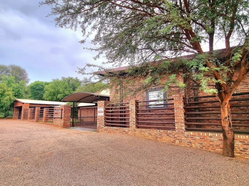 Front exterior view of a farm property featuring a face brick facade, timber slat fencing, and a gravel driveway entrance.