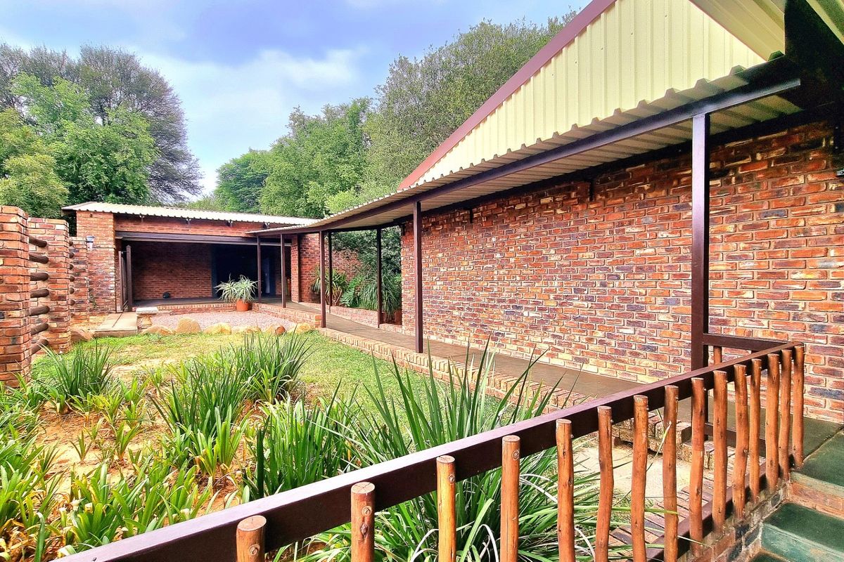 A well-maintained rear exterior view of the farm property featuring exposed brick walls, a covered walkway, and a landscaped garden area.