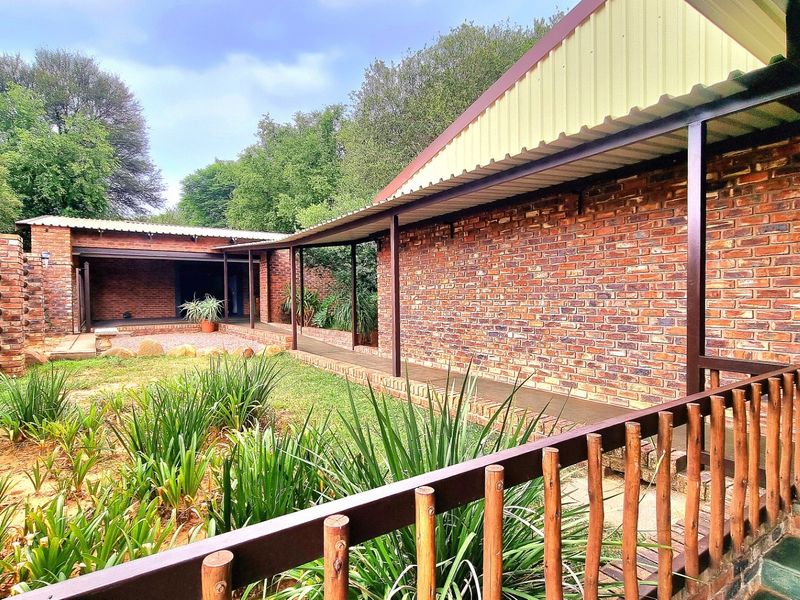 A well-maintained rear exterior view of the farm property featuring exposed brick walls, a covered walkway, and a landscaped garden area.