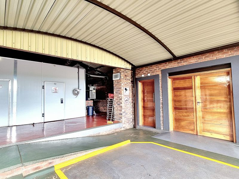 A functional utility and loading area featuring industrial cold storage access, double timber doors, and a concrete loading ramp under a covered roof structure.