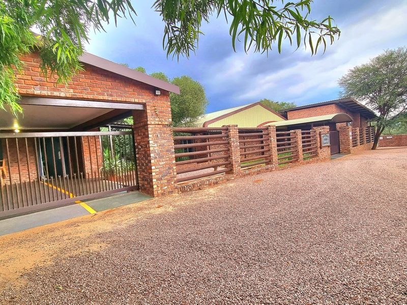 Front exterior view of a farm property featuring a face brick facade, gravel driveway, and secure gated entrance with covered parking.